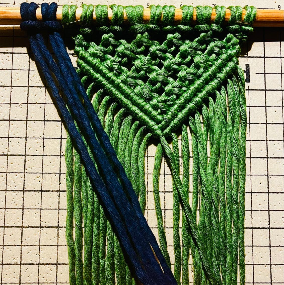 Macrame wall hanging with green and blue strings on a grid background