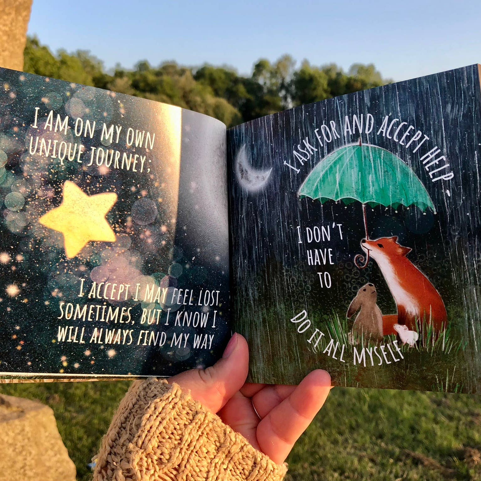 Open book with motivational quotes held by a person outdoors.