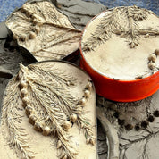 Decorative soap with leaf design next to a red container on a textured surface