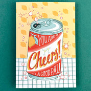 Illustrated can of 'Cheers!' with text on a yellow background