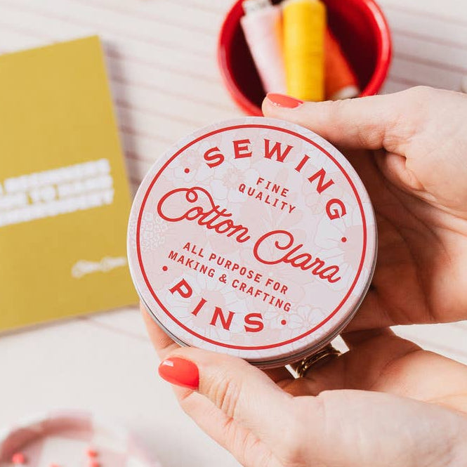 Person holding a container of sewing pins with a white background