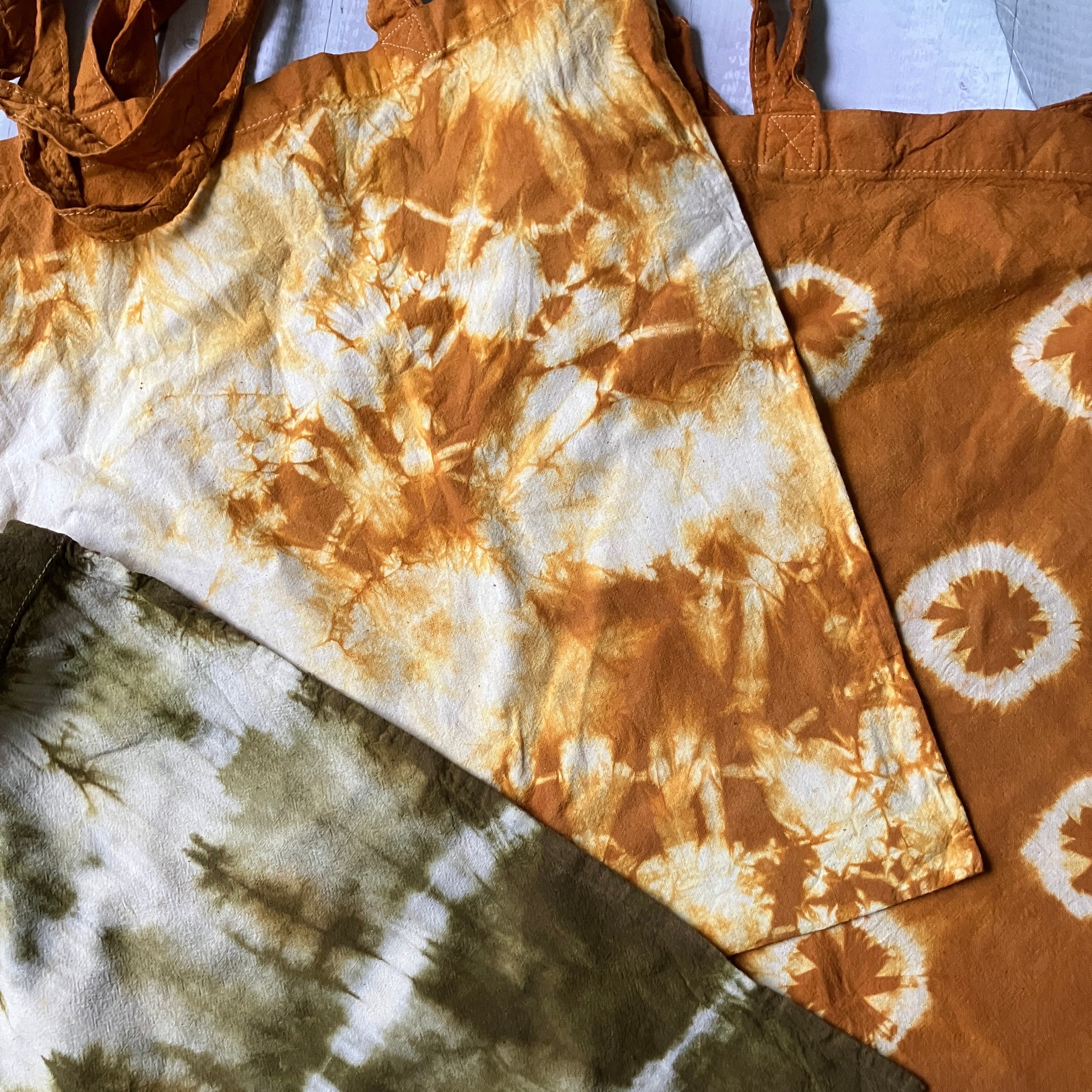 Three tie-dye fabric samples in brown, white, and black on a textured surface.
